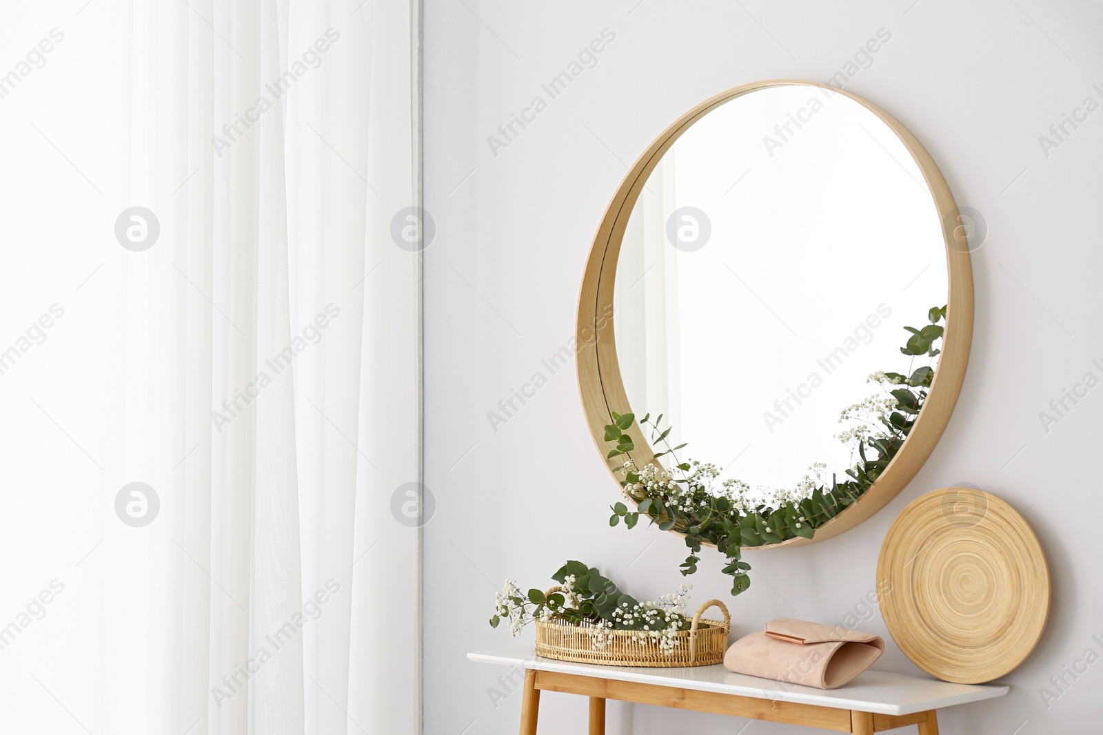 Photo of Round mirror and table with accessories near white wall. Modern interior design