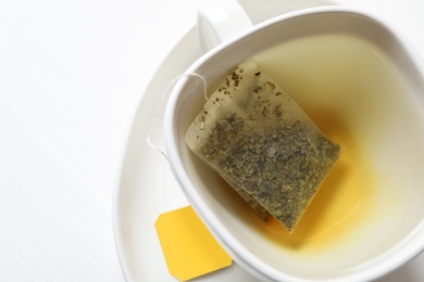 Photo of Tea bag in cup with water on white table, top view. Space for text