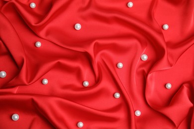 Photo of Many beautiful pearls on delicate red silk, top view