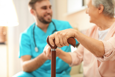 Photo of Medical worker taking care of elderly woman in geriatric hospice, focus on hand with stick