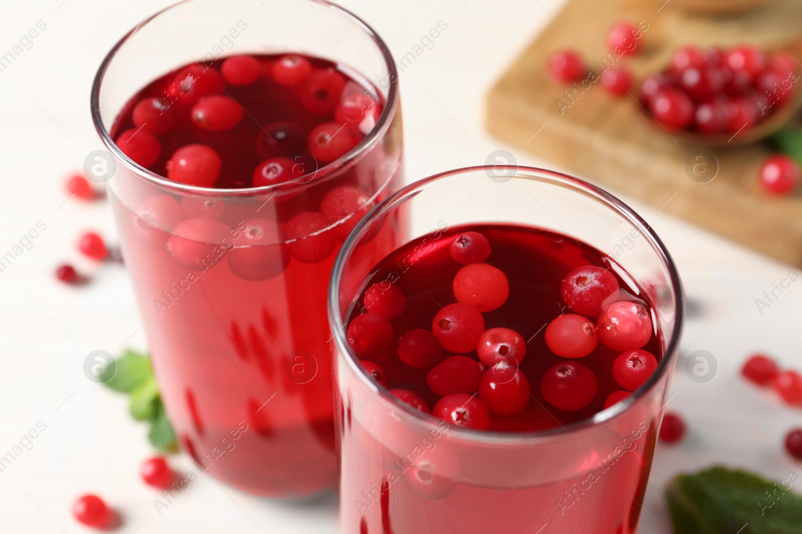 Photo of Tasty cranberry juice in glasses and fresh berries on white wooden table, closeup