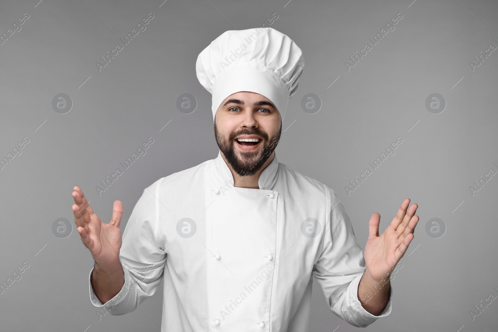 Photo of Excited young chef in uniform on grey background