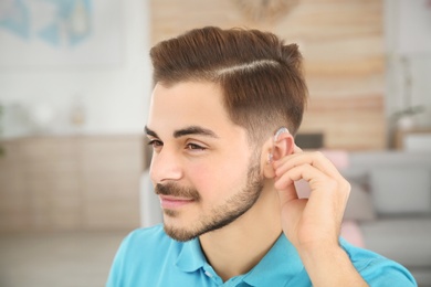 Young man adjusting hearing aid at home