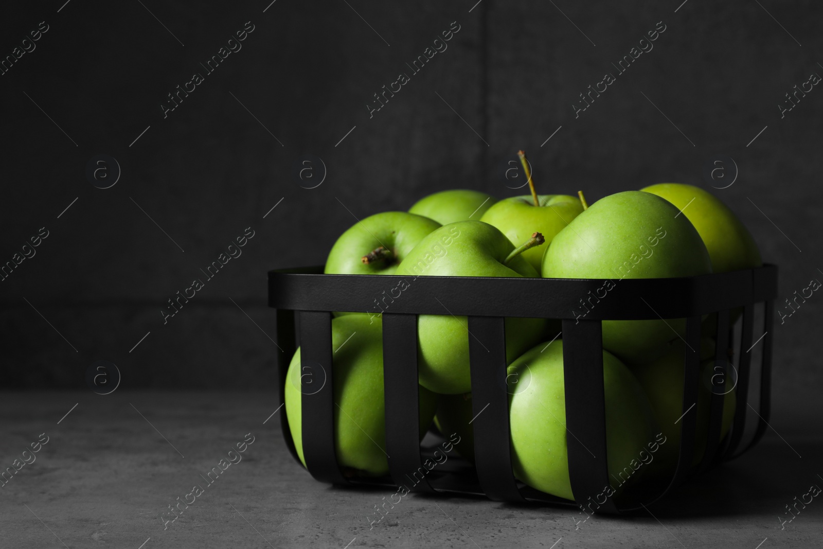 Photo of Black metal container full of apples on table against dark grey background, space for text