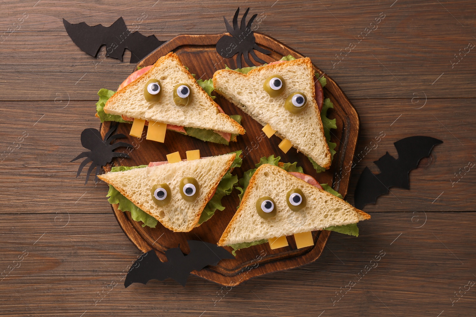 Photo of Tasty monster sandwiches and Halloween decorations on wooden table, flat lay