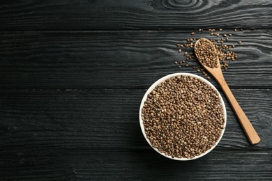 Ceramic bowl with chia seeds on black wooden table, flat lay and space for text. Cooking utensils