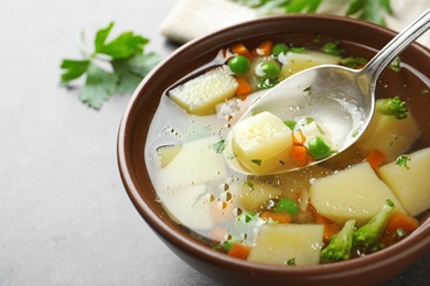 Photo of Spoon of fresh homemade vegetable soup over full bowl on grey table, closeup