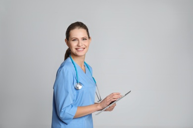 Portrait of young medical assistant with stethoscope and tablet on color background. Space for text