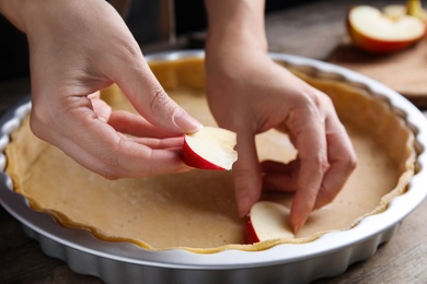 Photo of Woman putting apple slice into baking dish with dough to make traditional English pie at wooden table, closeup