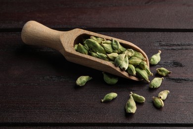 Scoop with dry cardamom pods on wooden table