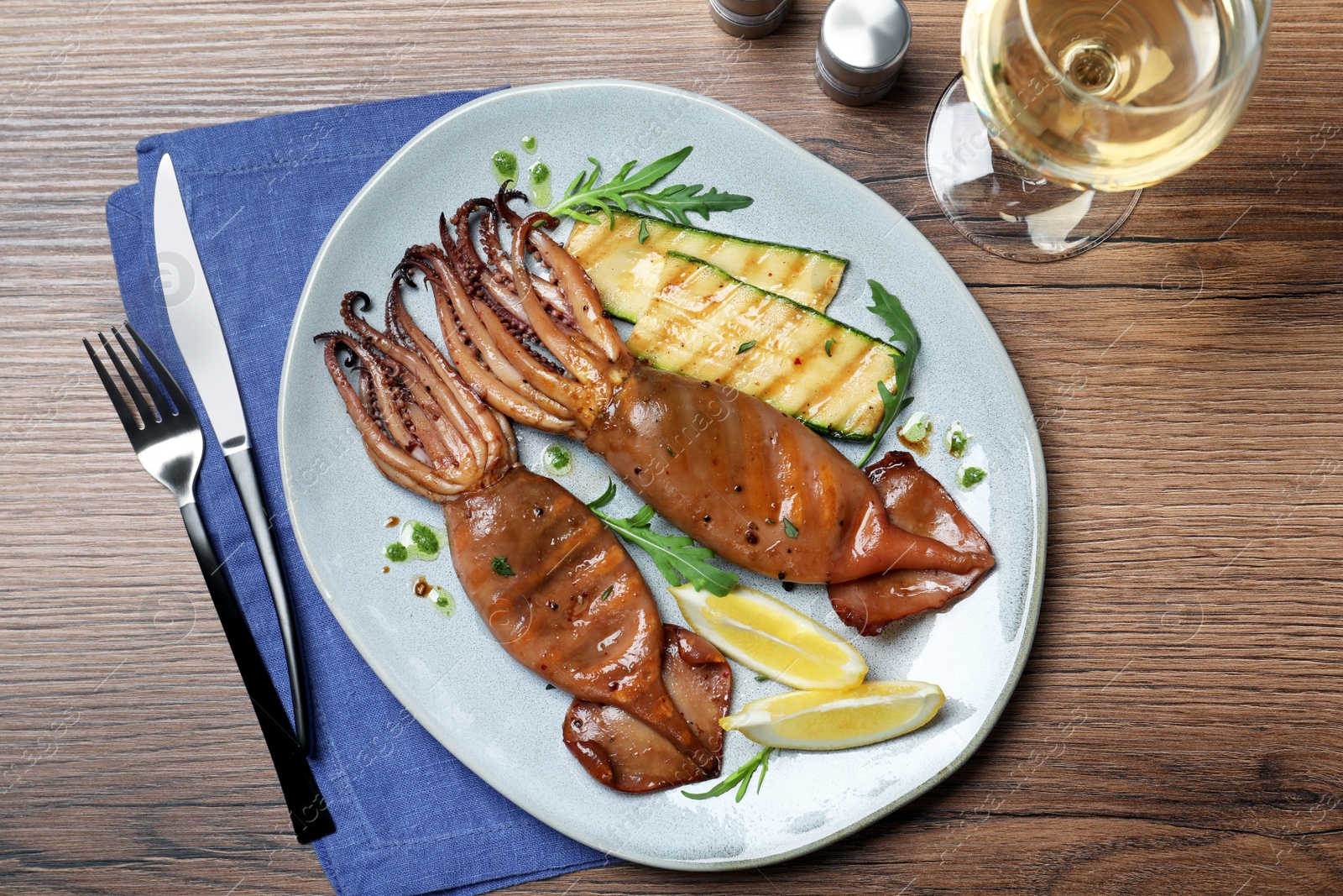 Photo of Delicious grilled squids served on wooden table, flat lay