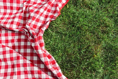 Photo of Checkered picnic tablecloth on fresh green grass, top view. Space for text