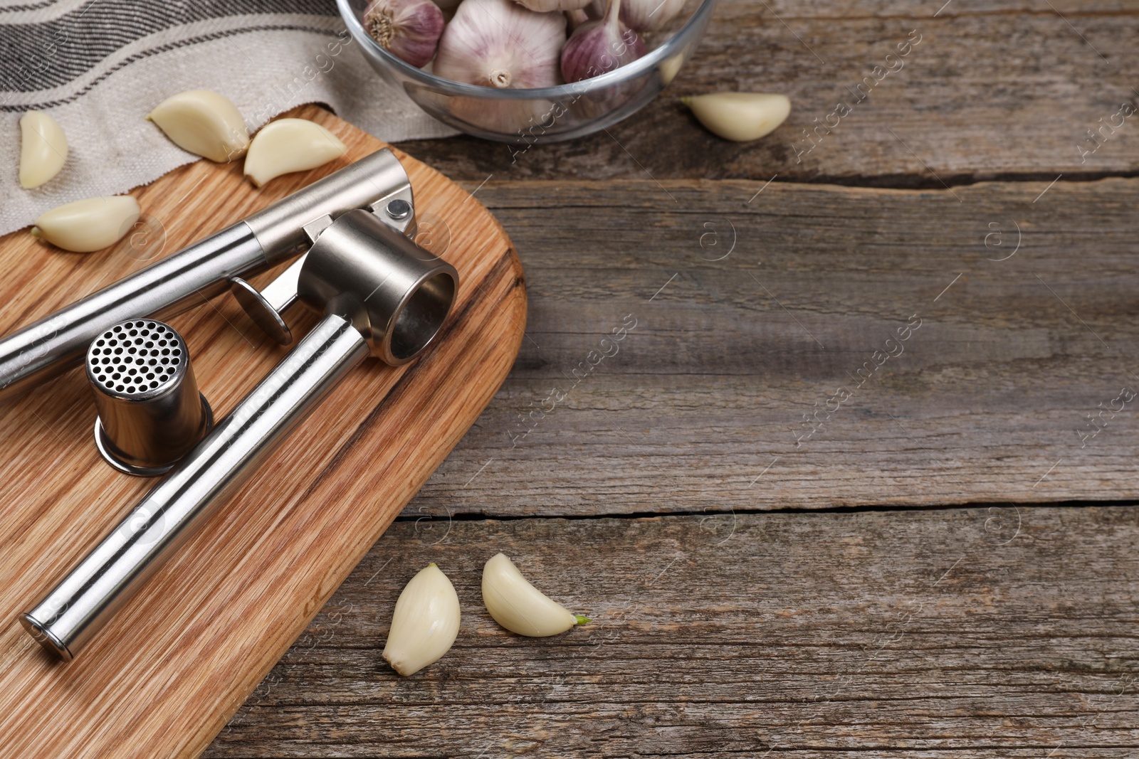Photo of Garlic press and cloves on wooden table. Space for text