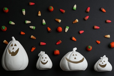 Photo of Jack-o-Lantern candle holders and jelly candies on black background, flat lay. Halloween decor