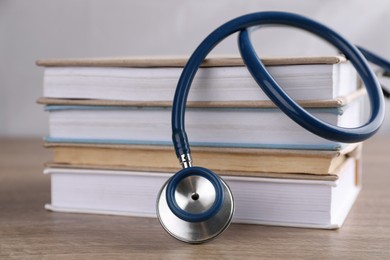Photo of Stack of student textbooks and stethoscope on wooden table, closeup. Medical education