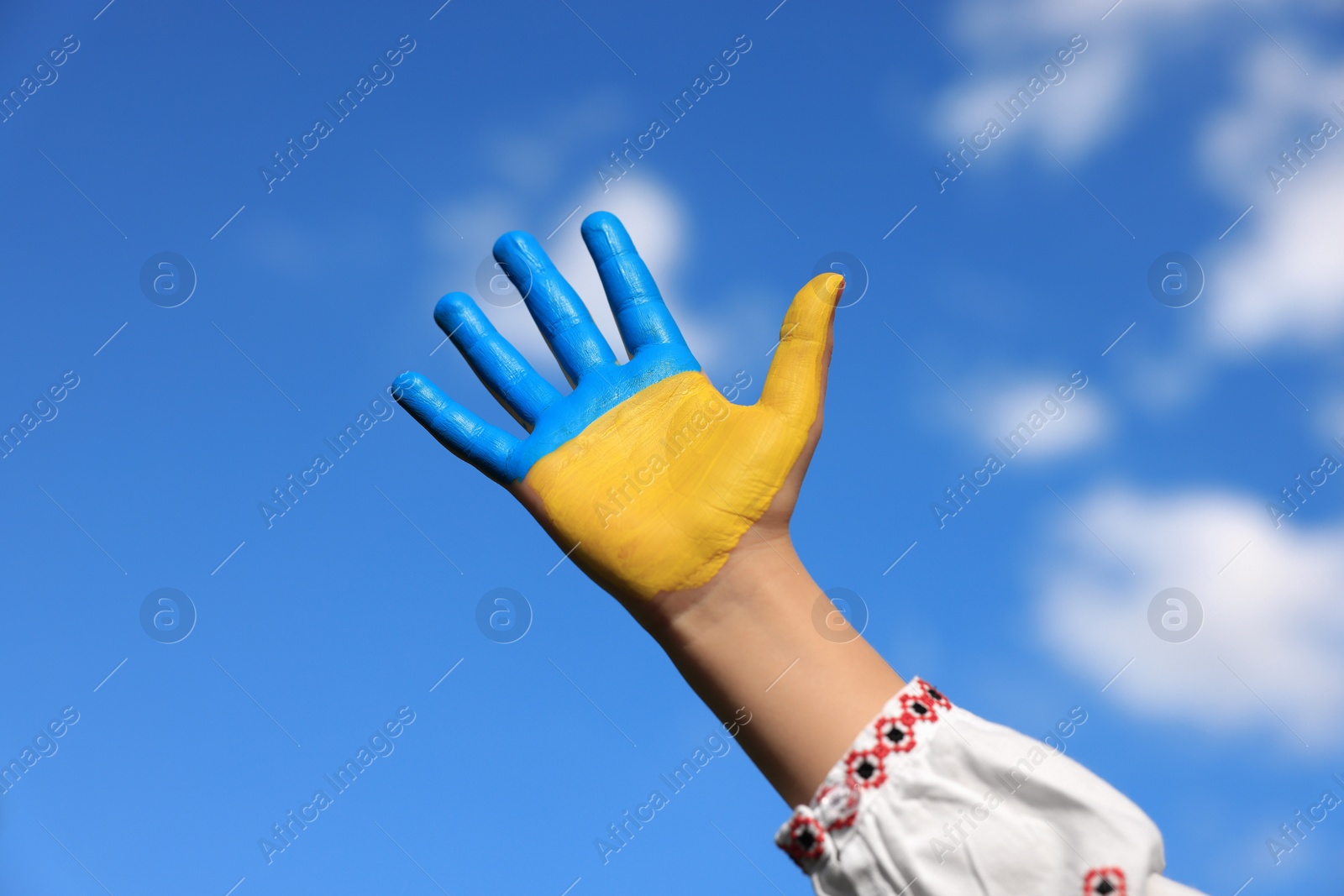 Photo of Little girl with hand painted in Ukrainian flag colors against blue sky, closeup. Love Ukraine concept