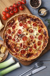 Delicious homemade prosciutto quiche, ingredients and cutlery on gray wooden table, flat lay