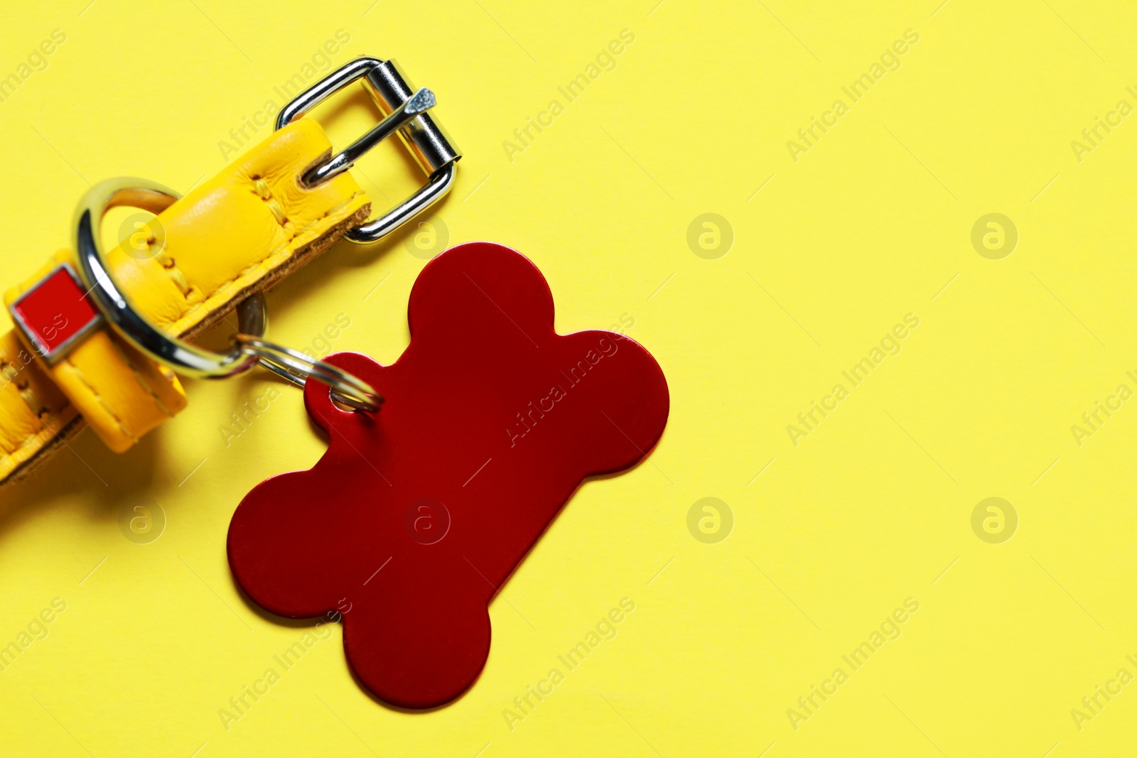 Photo of Leather dog collar with red tag in shape of bone on yellow background, flat lay. Space for text