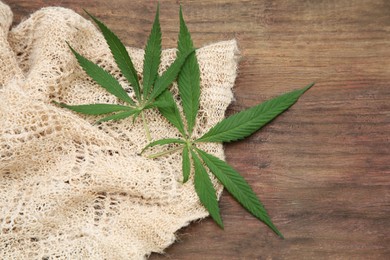 Photo of Hemp cloth and green leaves on wooden table, top view. Space for text