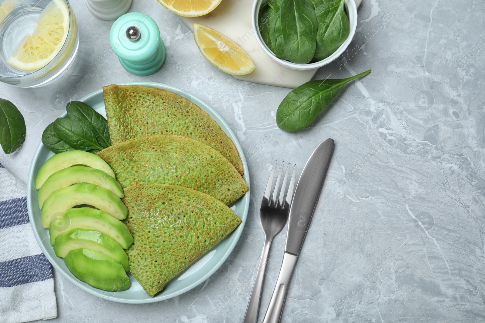 Photo of Delicious spinach crepes with avocado served on marble table, flat lay