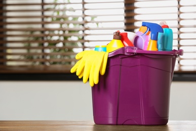 Plastic bucket with different cleaning products on table indoors, space for text