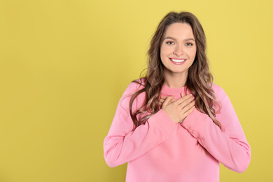 Beautiful grateful woman with hands on chest against yellow background. Space for text