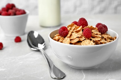 Photo of Bowl with cornflakes and raspberries on gray table. Whole grain cereal for breakfast