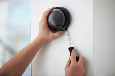 Photo of Technician installing CCTV camera on wall indoors, closeup