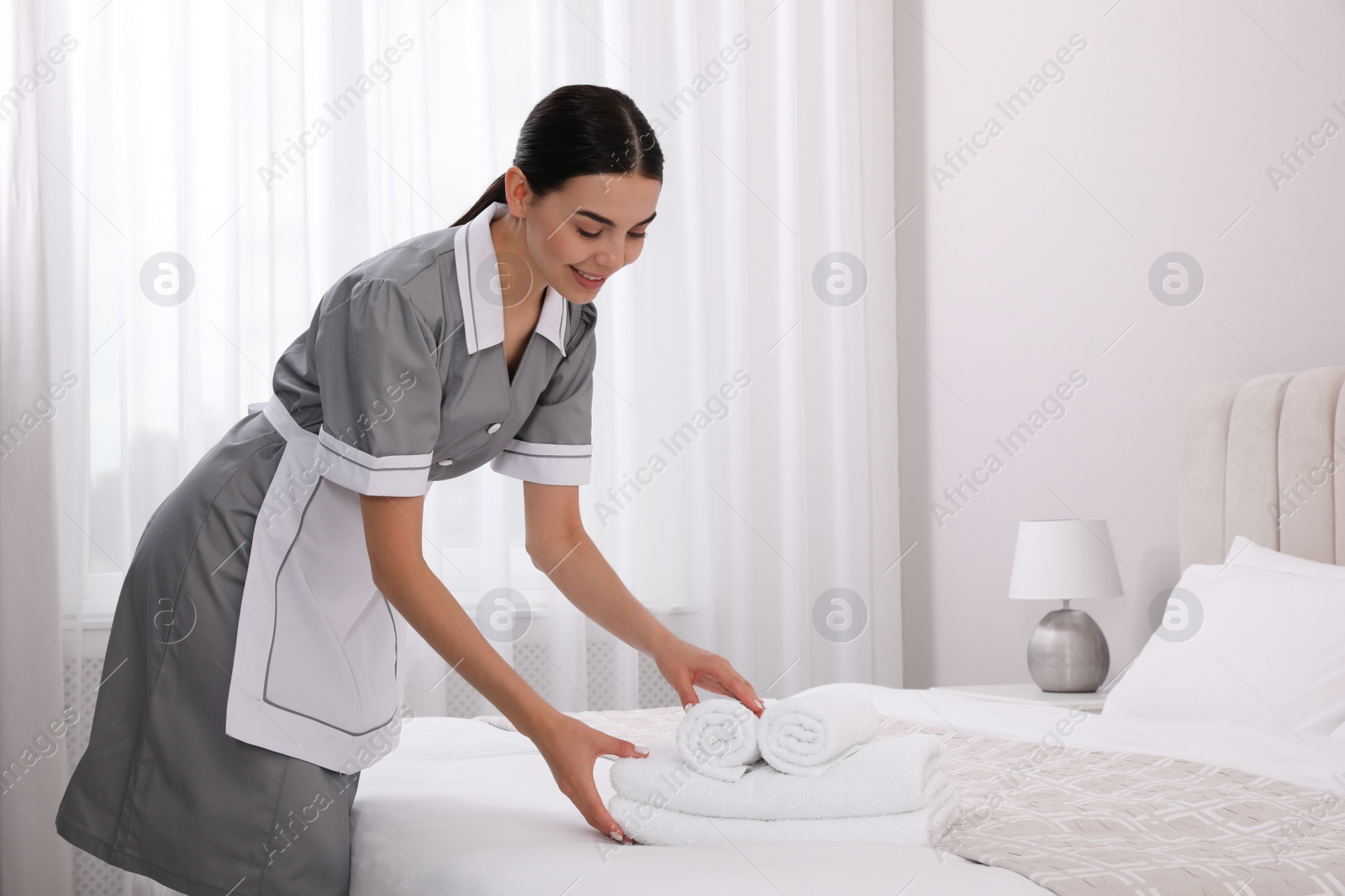 Photo of Chambermaid putting fresh towels on bed in hotel room, space for text