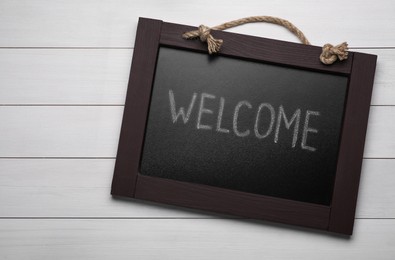 Small chalkboard with word Welcome on white wooden background, top view