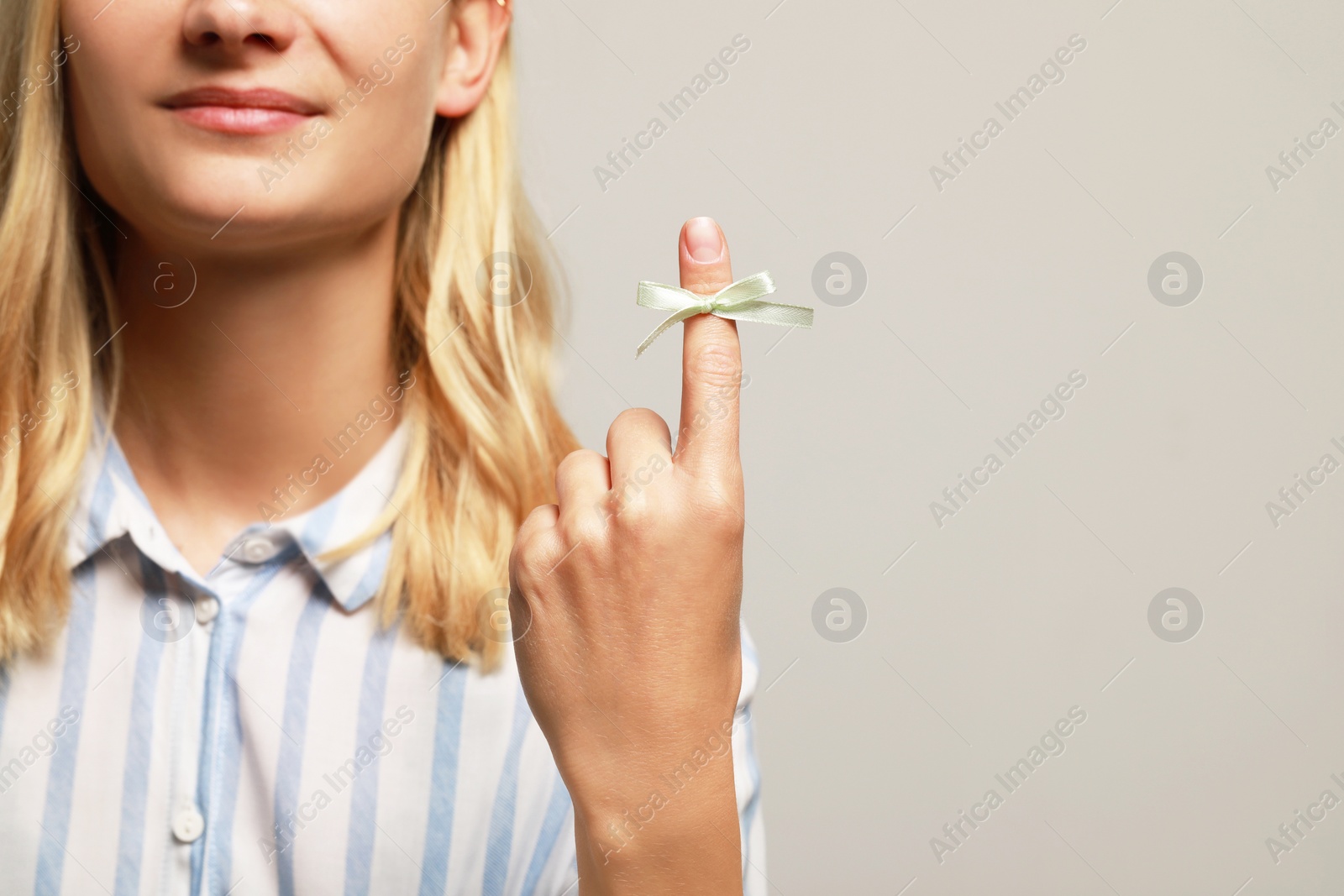 Photo of Woman showing index finger with tied bow as reminder on grey background, closeup. Space for text