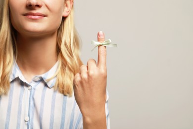 Photo of Woman showing index finger with tied bow as reminder on grey background, closeup. Space for text