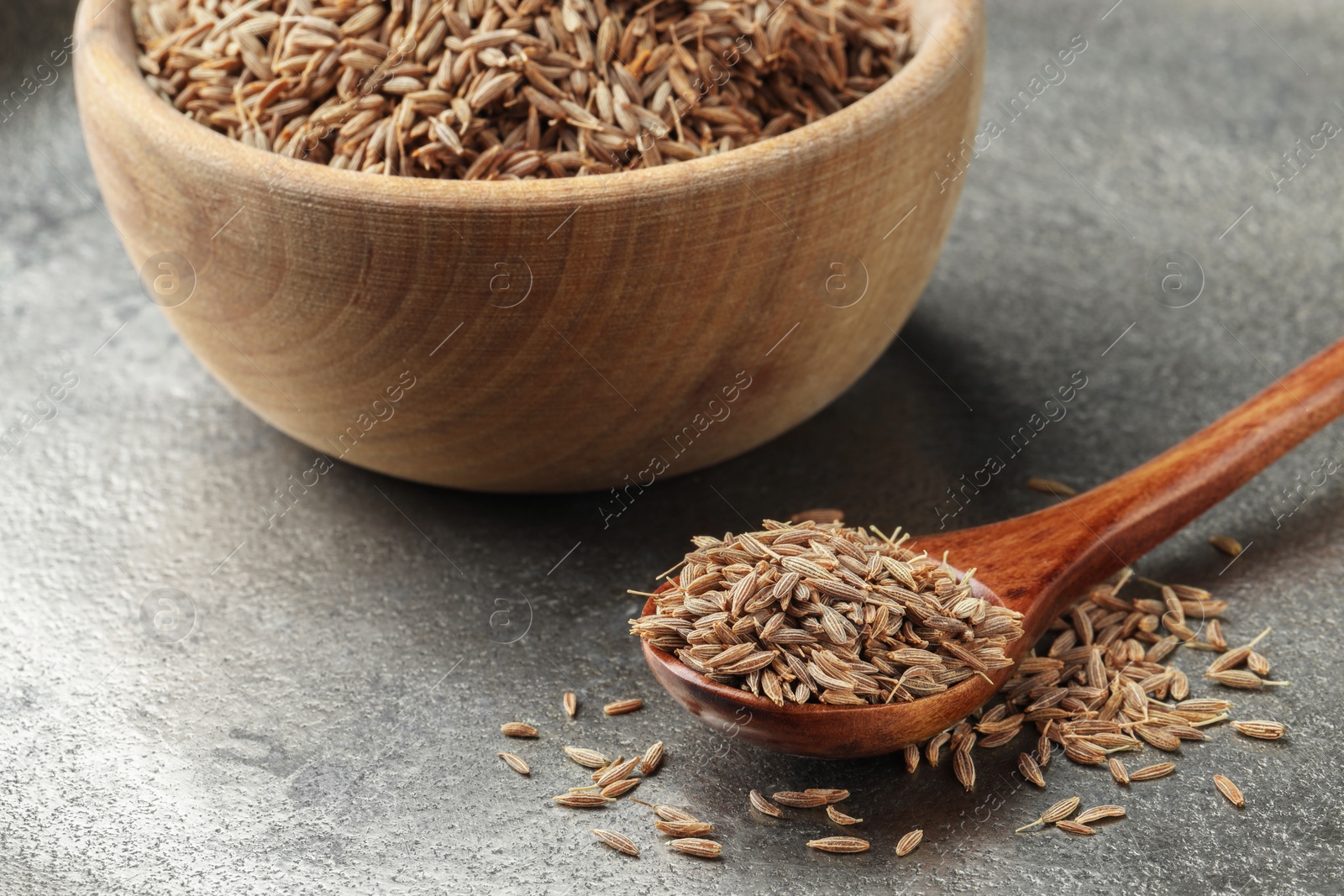 Photo of Spoon and bowl with caraway seeds on grey table, closeup