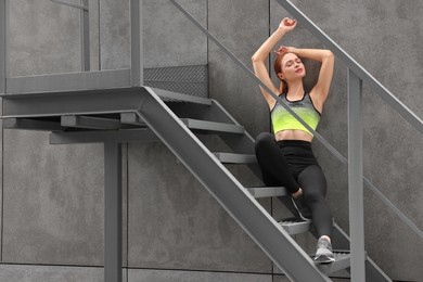 Photo of Beautiful woman in stylish gym clothes sitting on stairs on street