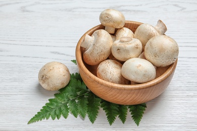 Bowl with fresh champignon mushrooms on wooden background, space for text