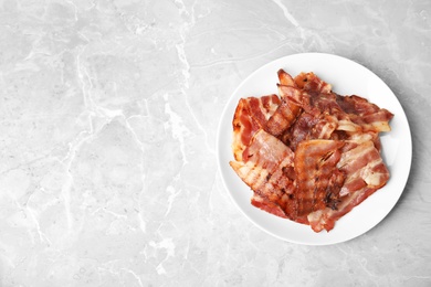 Photo of Slices of tasty fried bacon on light marble table, top view. Space for text