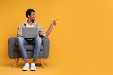 Photo of Happy man with laptop sitting in armchair on orange background. Space for text