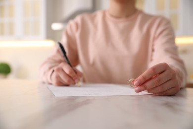 Photo of Woman with wedding ring signing divorce papers at table indoors, closeup. Space for text