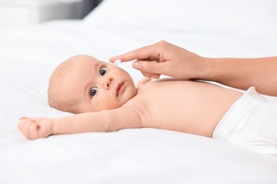 Photo of Woman applying cream onto baby`s face on bed, closeup