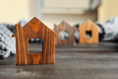 Photo of Wooden house model and scarf on grey table, space for text. Heating efficiency