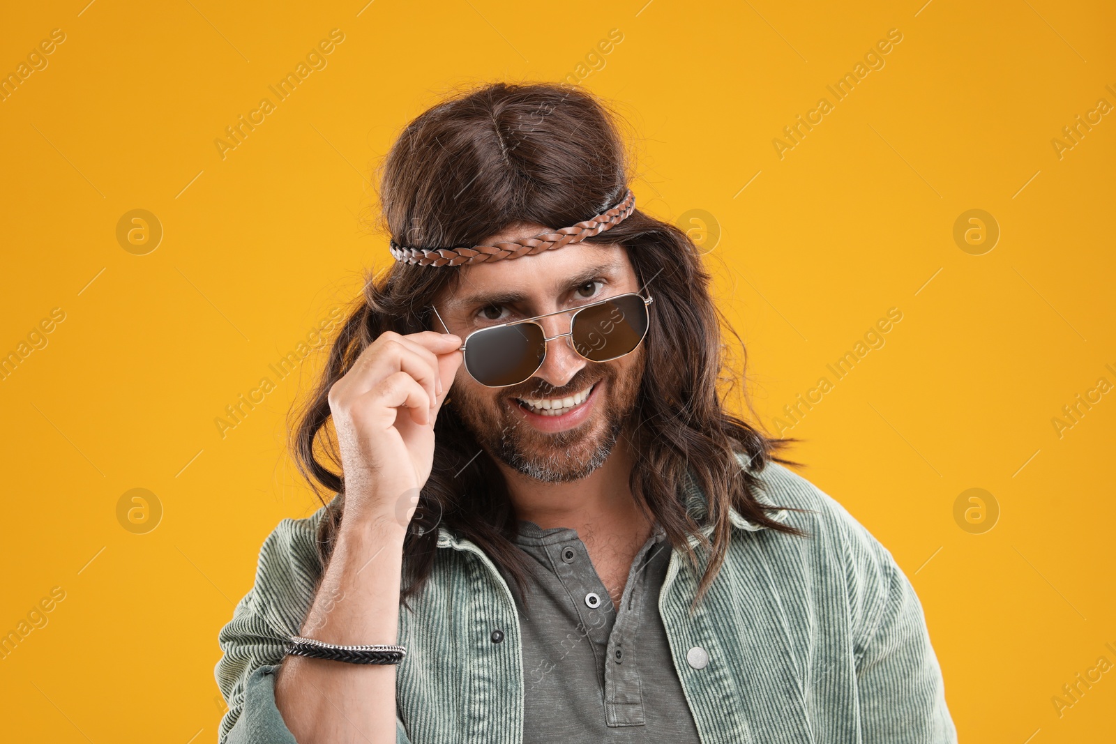 Photo of Stylish hippie man in sunglasses on orange background