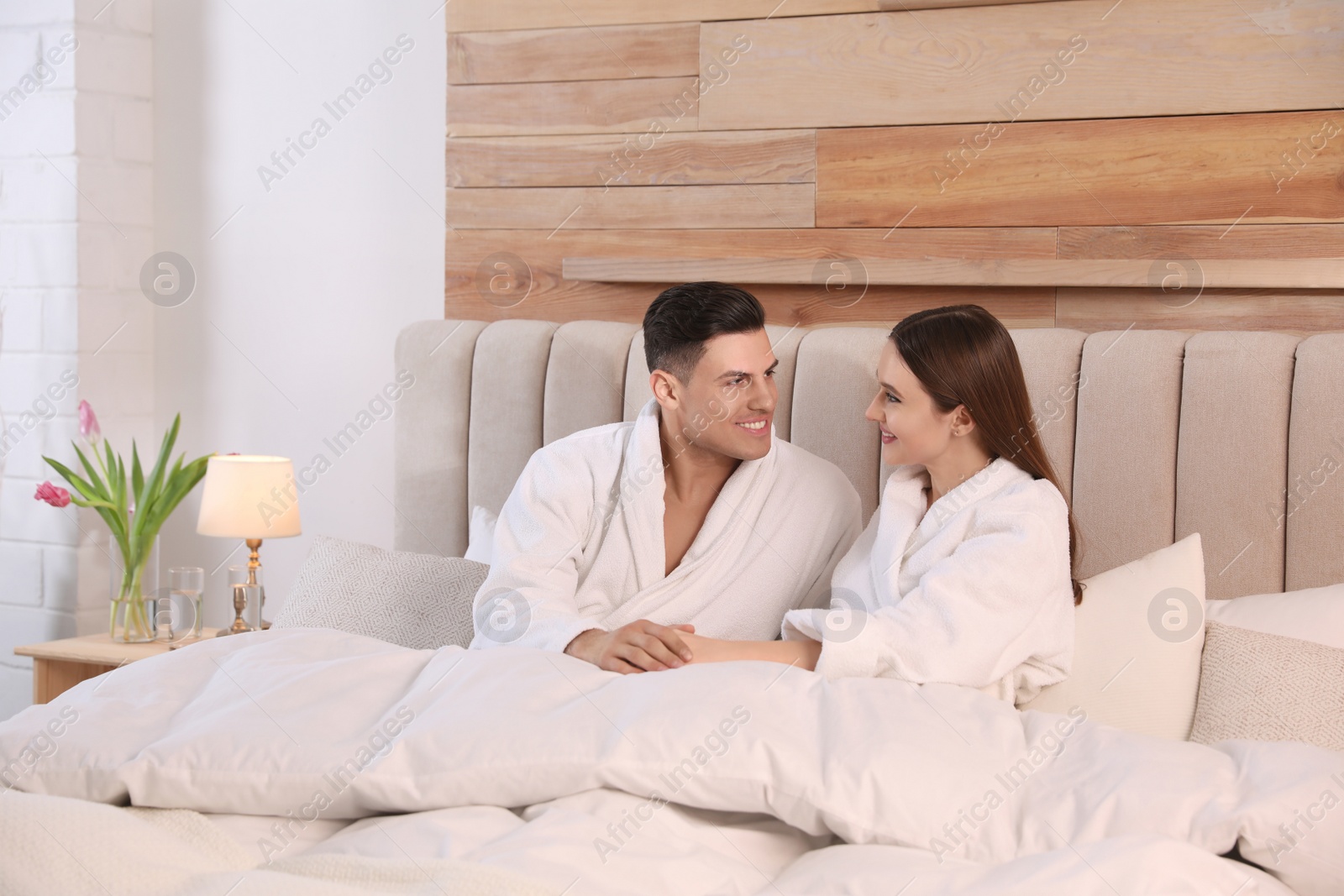 Photo of Happy couple in bathrobes resting on bed at home