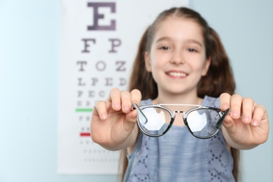 Photo of Cute little girl with eyeglasses in ophthalmologist office