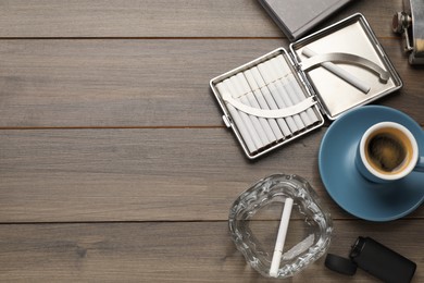 Photo of Case with tobacco filter cigarettes, glass ashtray and cup of coffee on wooden table, flat lay. Space for text