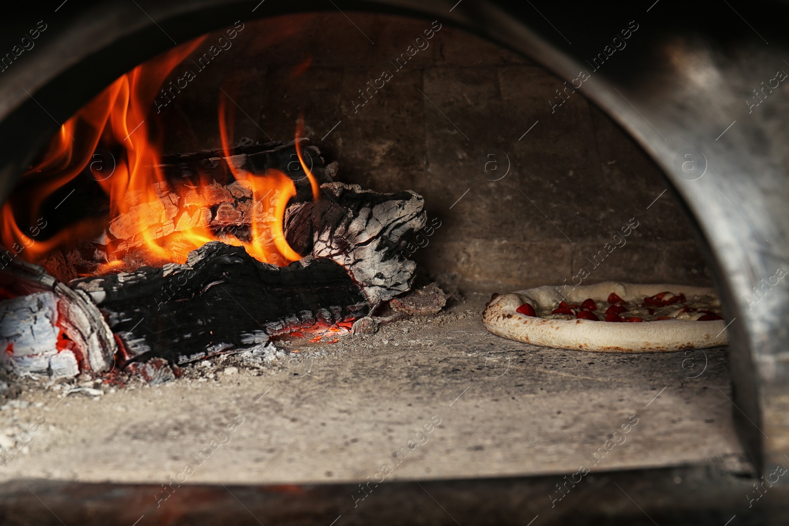 Photo of Oven with burning firewood and tasty pizza in restaurant kitchen