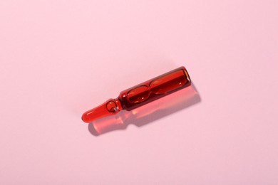 Photo of Glass ampoule with liquid on pink background, top view