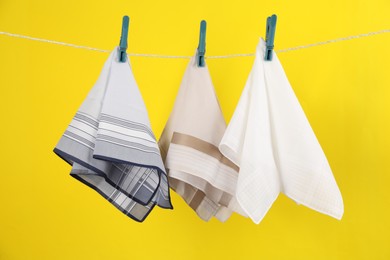 Photo of Many different handkerchiefs hanging on rope against yellow background