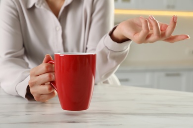 Photo of Woman with red cup at table indoors, closeup