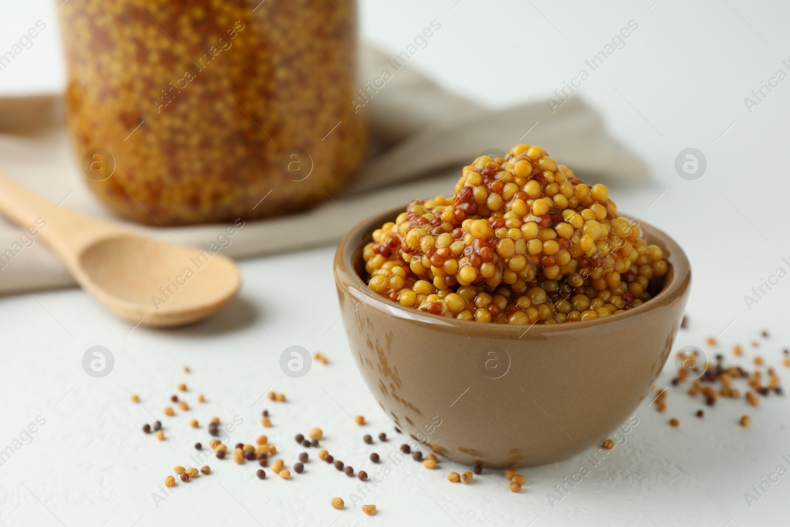 Photo of Fresh whole grain mustard in bowl and dry seeds on white table. Space for text