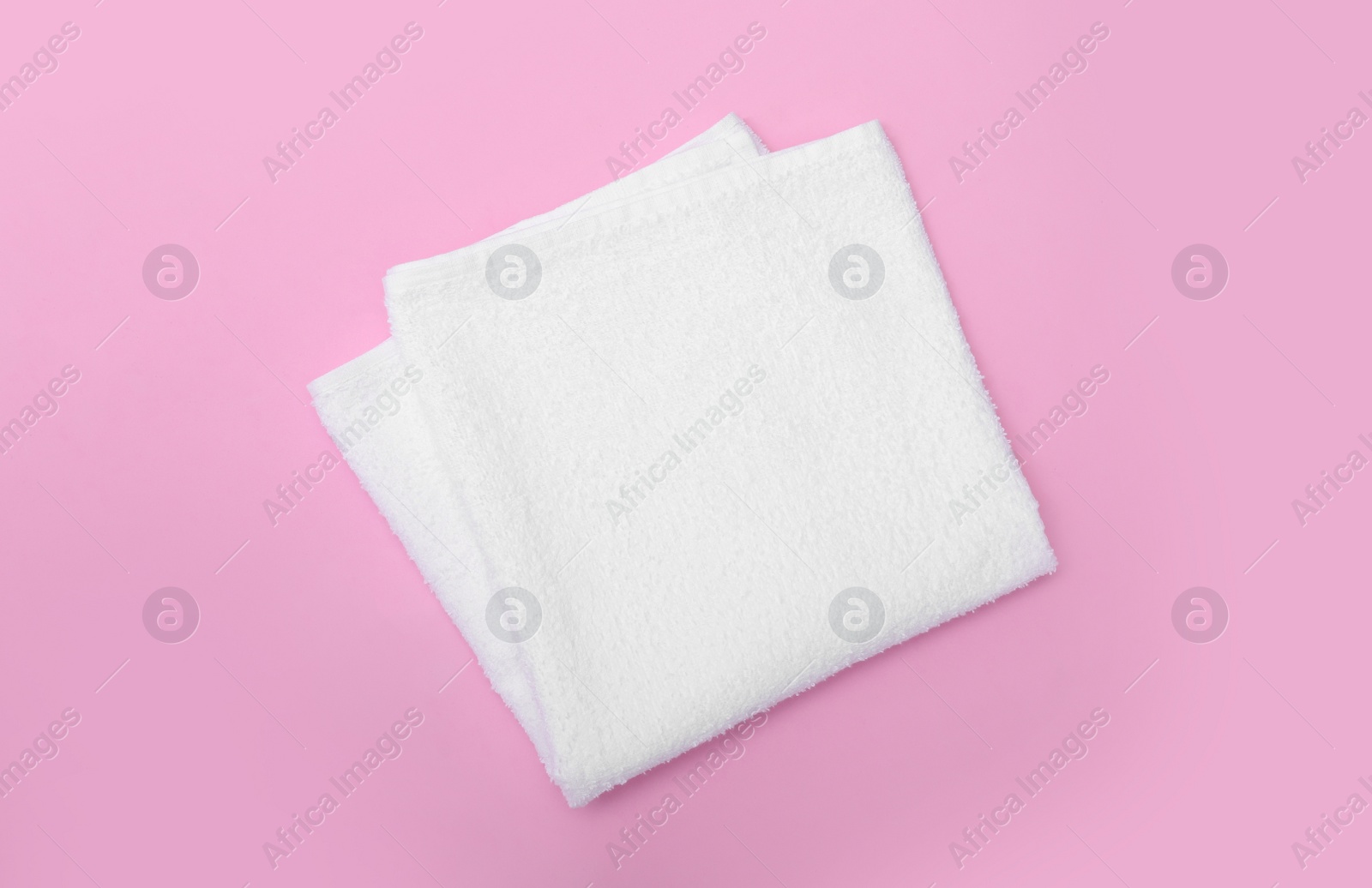 Photo of Folded white beach towel on pink background, top view